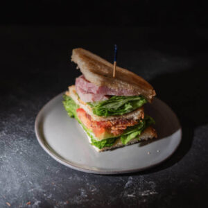 Sandwich gourmet sur assiette blanche - garni de jambon, laitue verte et tomate - création Goutéo