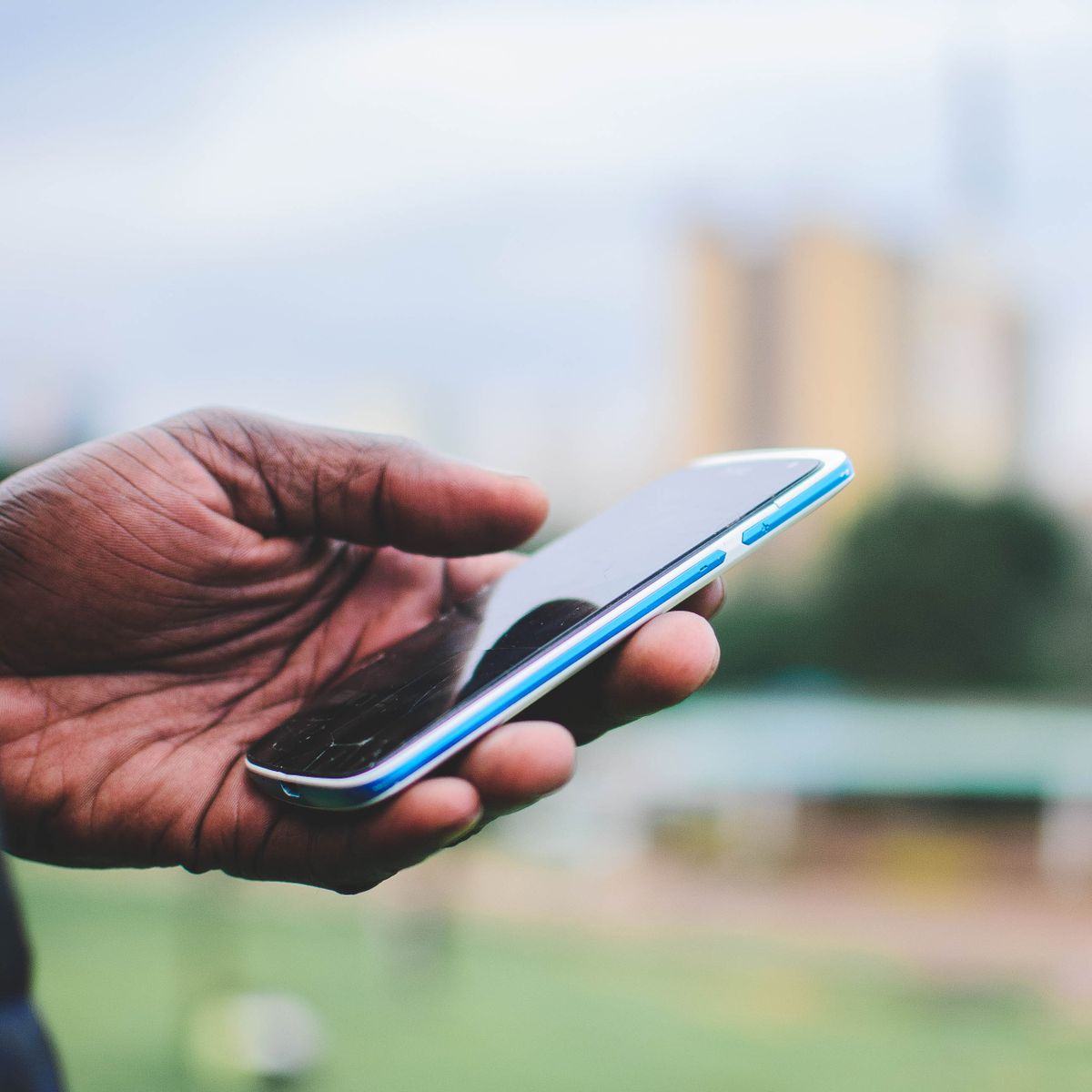 Une main tient un smartphone en extérieur pour commander en ligne, arrière-plan urbain flou