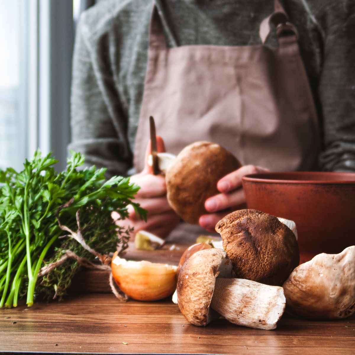 Chef en tablier préparant champignons et persil frais dans sa cuisine artisanale