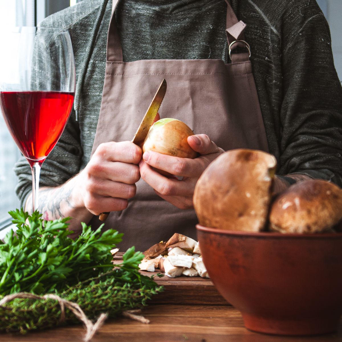 Chef en tablier hachant champignons et oignons frais avec des herbes en cuisine