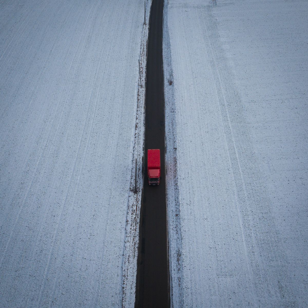 Camion rouge circulant sur une route de campagne enneigée traversant un paysage d'hiver rural