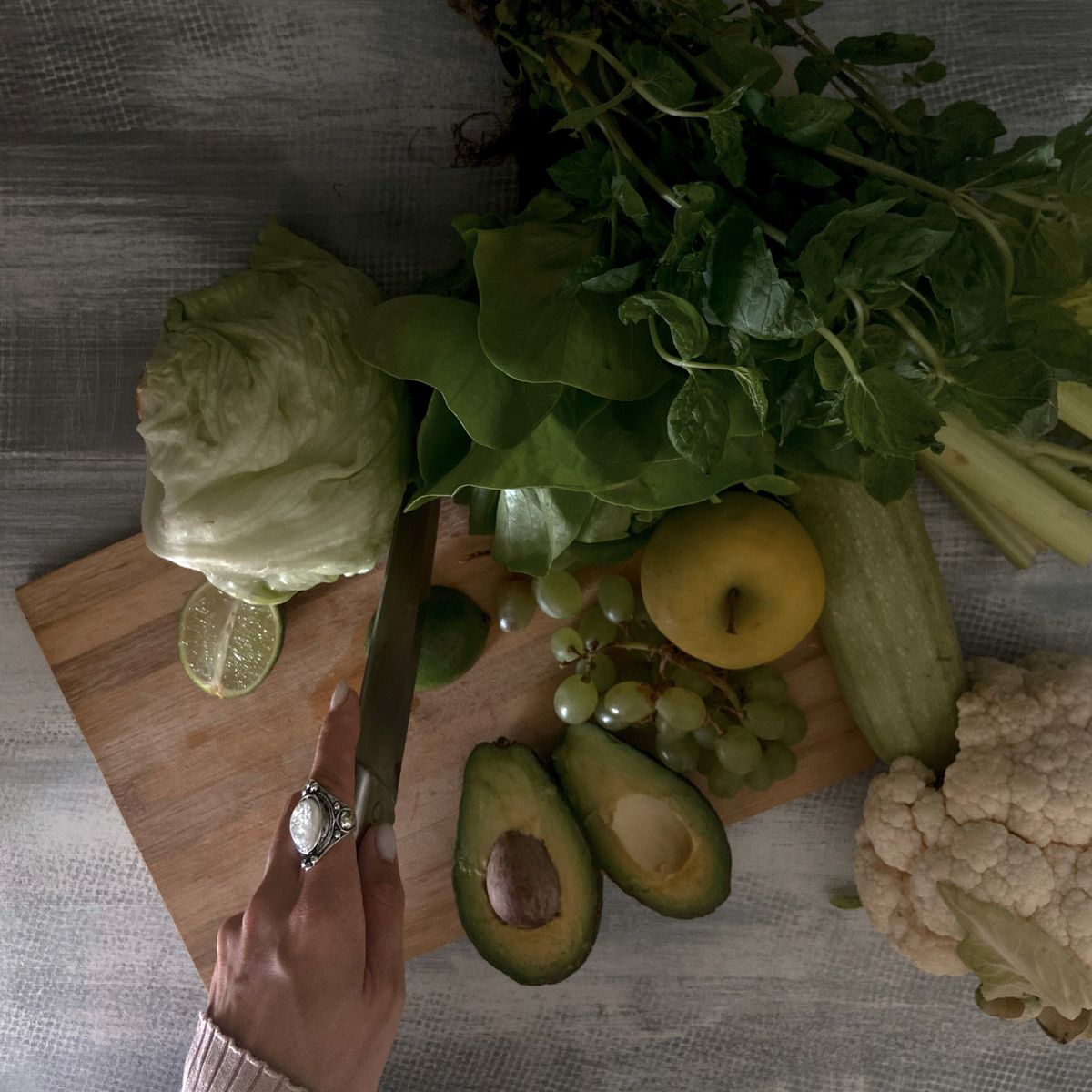 Une main découpe des légumes et fruits frais sur une planche en bois